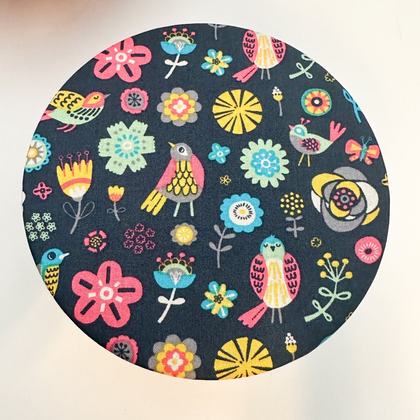 Round fabric swatch with colorful floral and bird pattern on a dark blue background