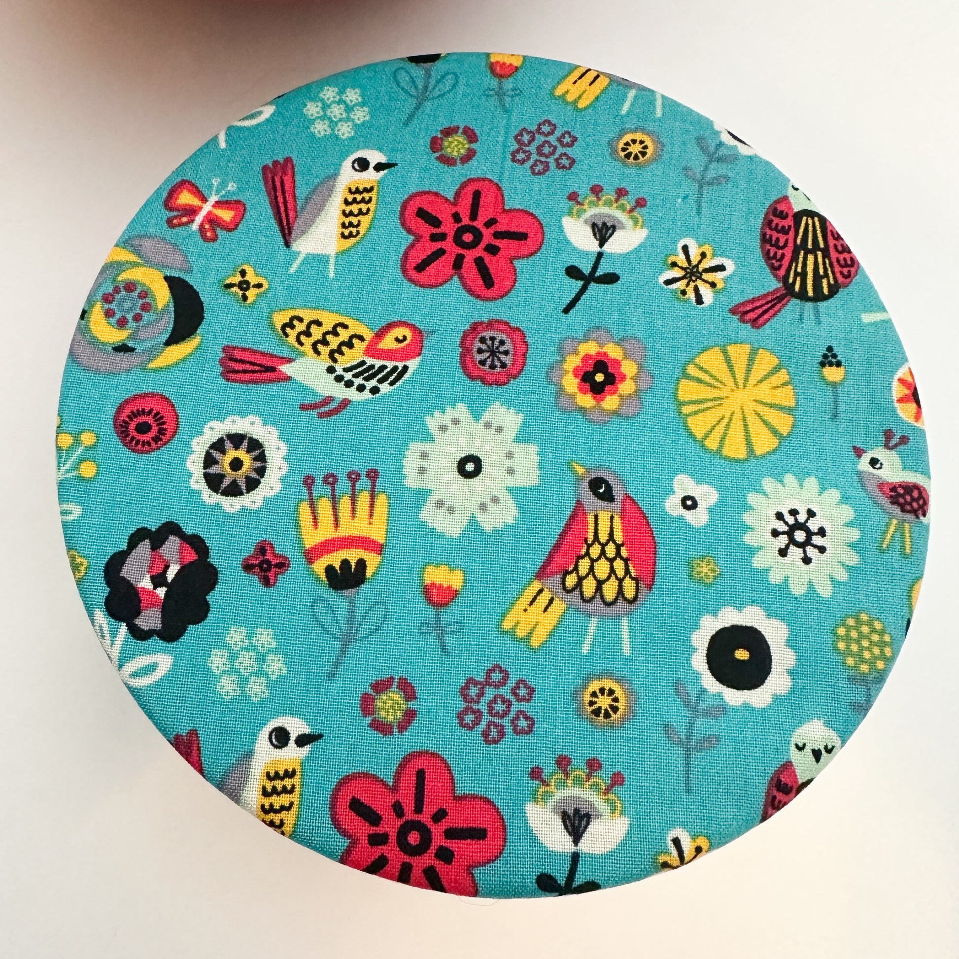 Round fabric sample with colorful bird and flower pattern on a blue background