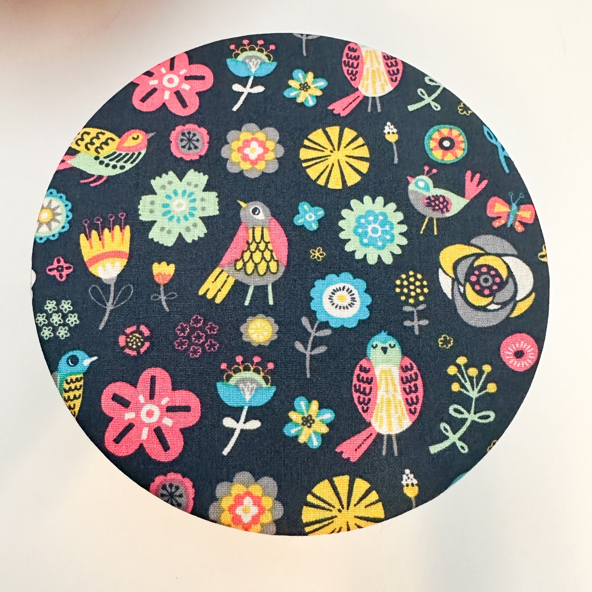 Round fabric swatch with colorful floral and bird pattern on a dark blue background