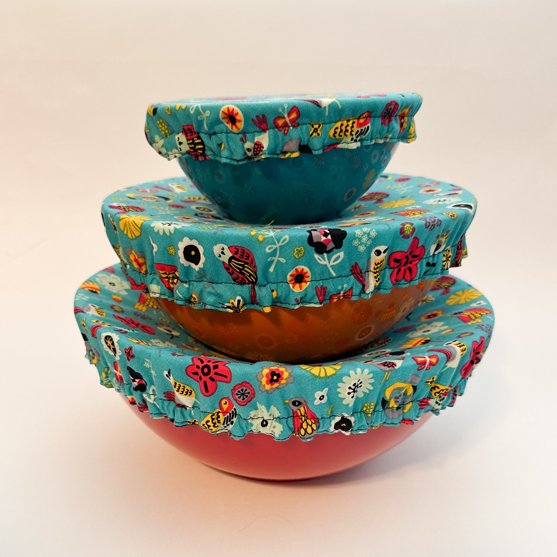 Stack of colorful ceramic bowls with floral lids on a beige background